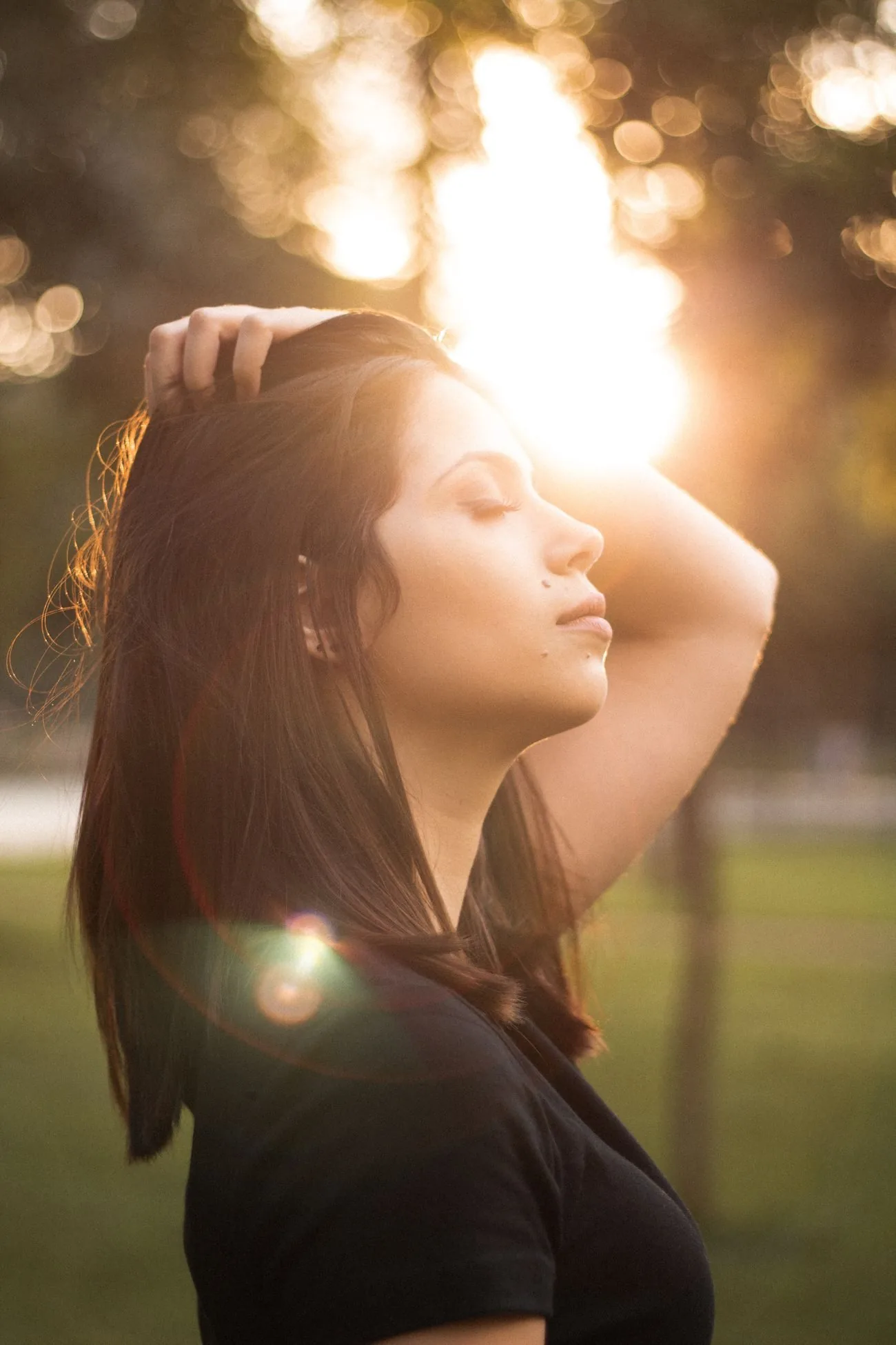 A woman standing outside in warm evening sunlight with her eyes closed.