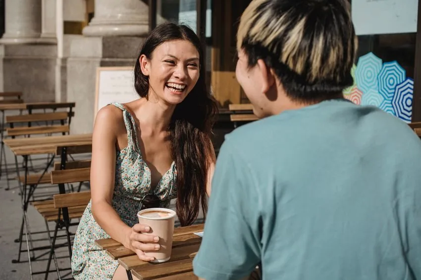 Two people laughing over coffee at an outdoor cafe table.