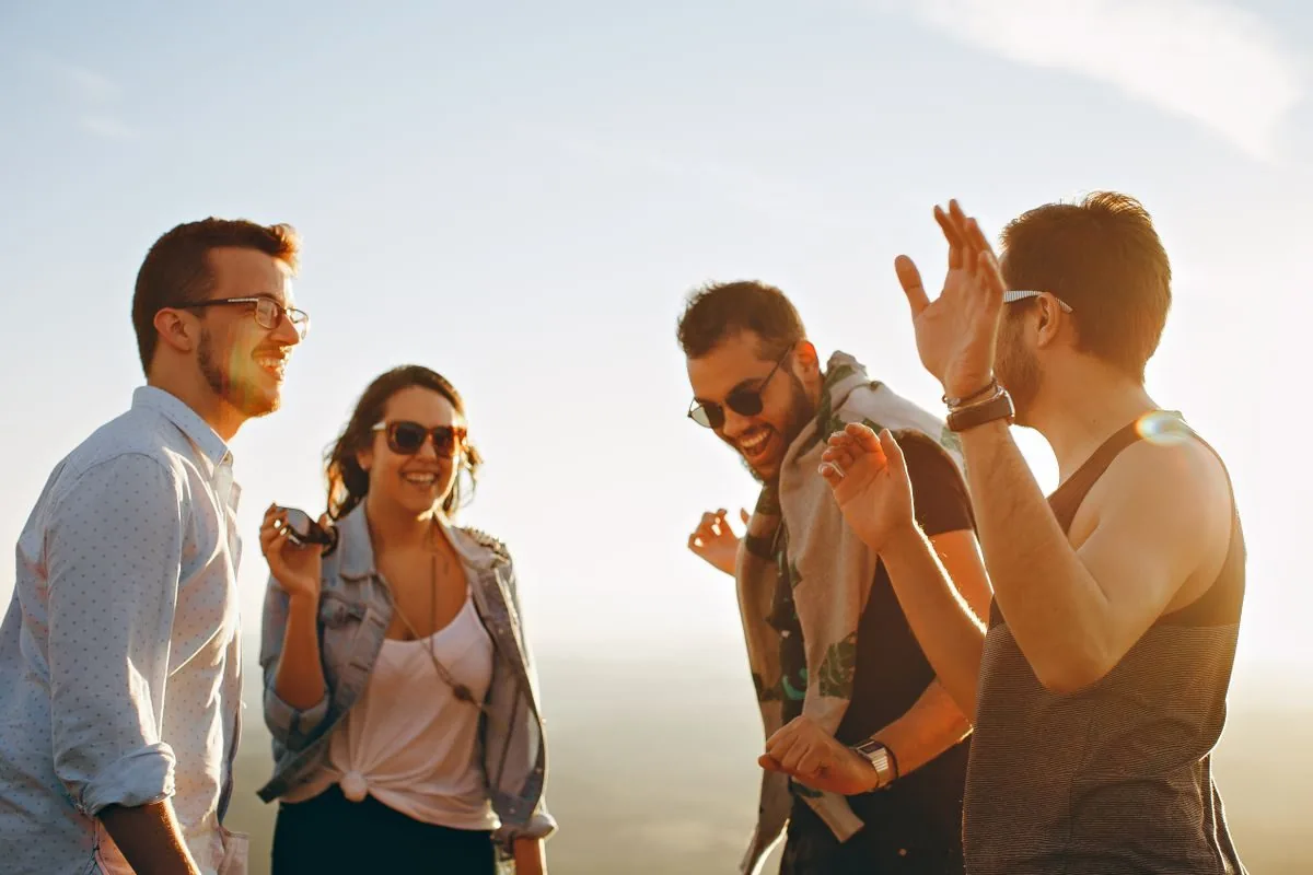 Four friends laughing together outdoors in low evening sun.